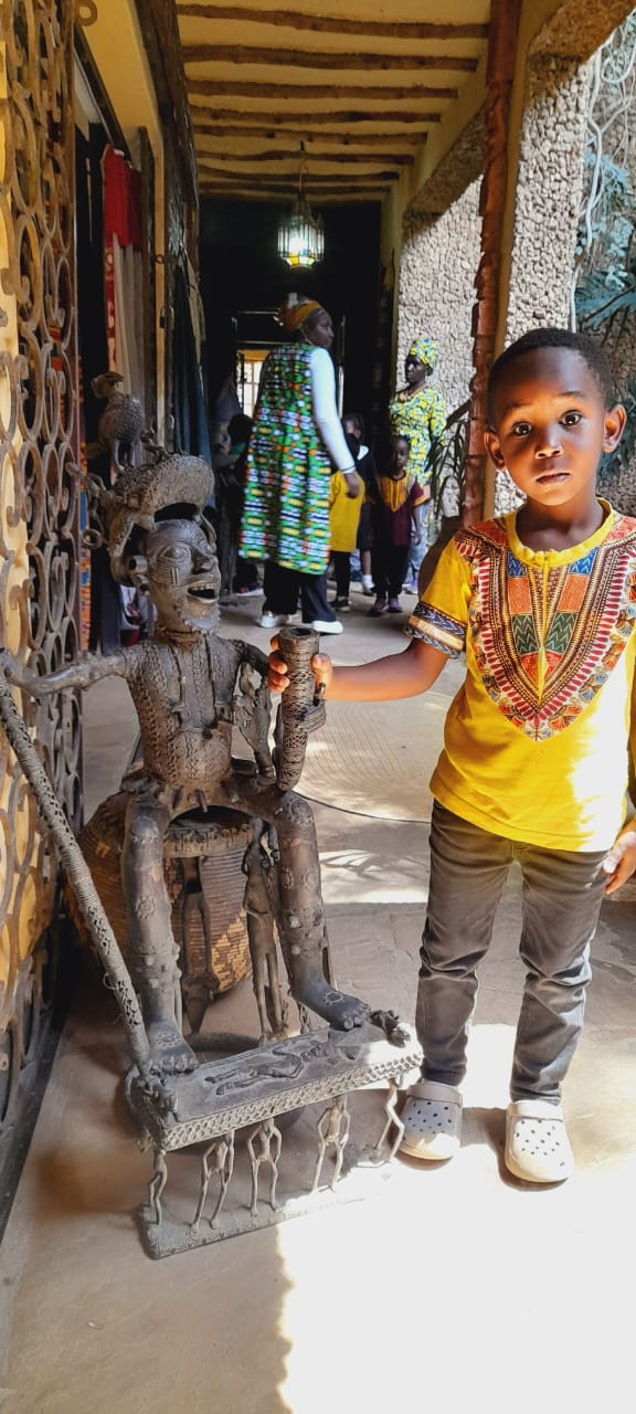 Young student in traditional African attire standing next to cultural artifacts