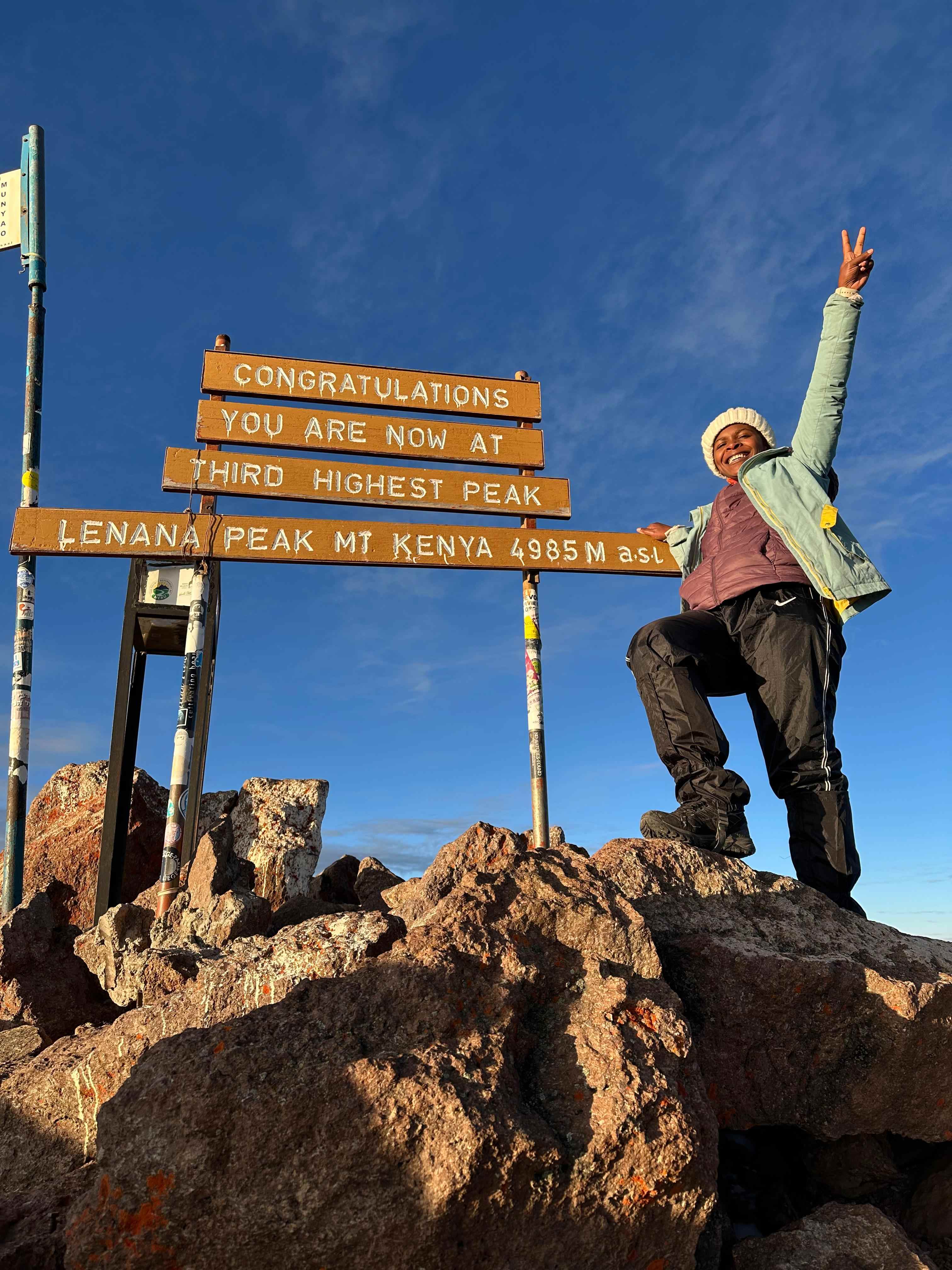 Ms. Wamaitha celebrating at the summit of Mt. Kenya (Lenana Peak, 4985m), demonstrating personal achievement and resilience